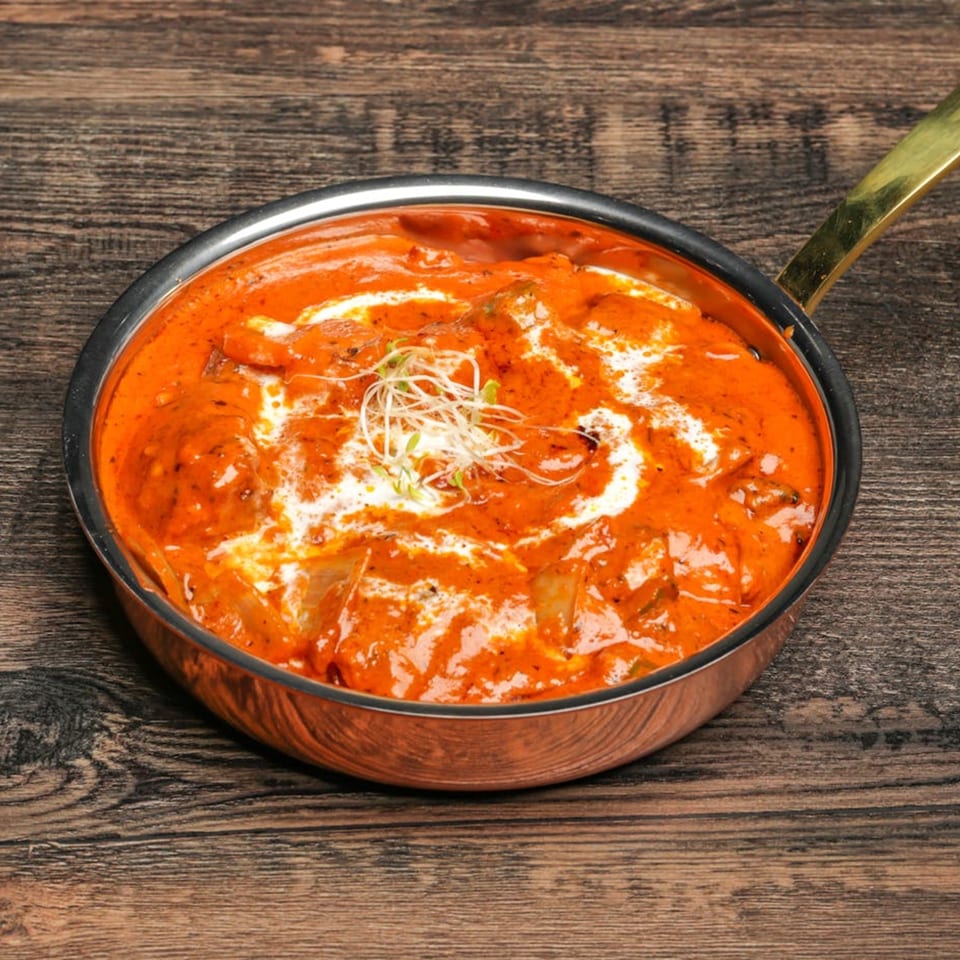 Vibrant orange Indian curry with cream swirls and microgreens in a copper pan on a wooden table.
