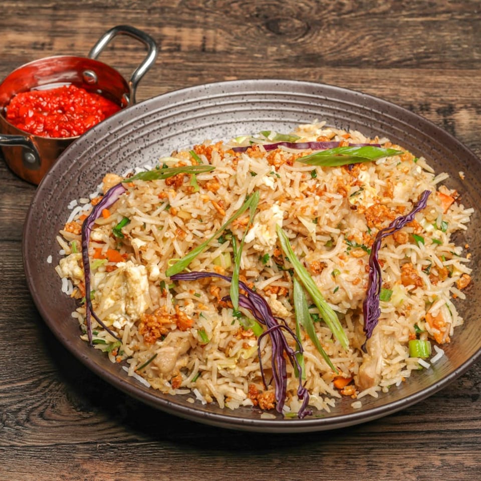 A plate of Indian fried rice with chicken, vegetables, and a side of red chili sauce.