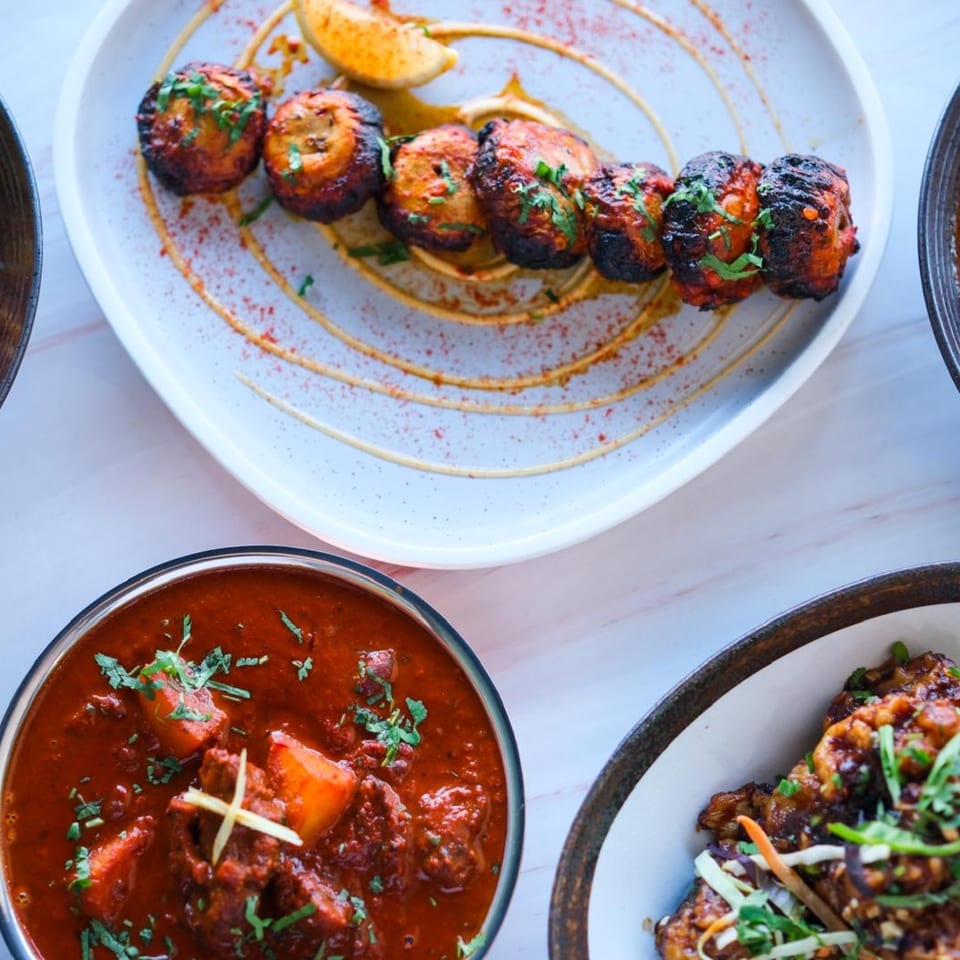 Overhead view of three Indian dishes: mushroom tikka, red curry, and chili chicken.