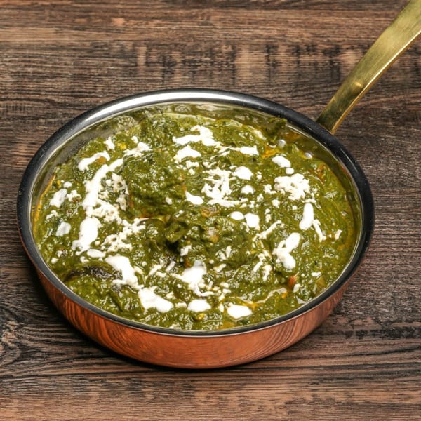 Palak Paneer, a vibrant green Indian spinach and cheese dish, in a copper pan on a wooden table.