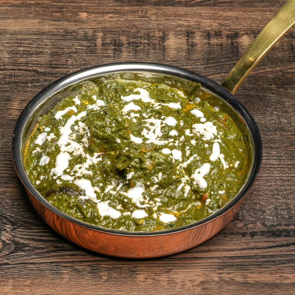 Palak Paneer, a vibrant green Indian spinach and cheese dish, in a copper pan on a wooden table.