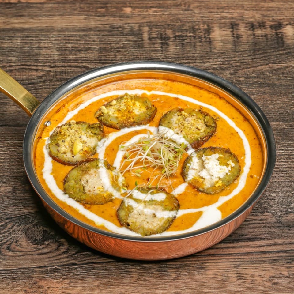 Indian curry with green vegetable slices, white cream swirls, and sprouts in a copper pan.