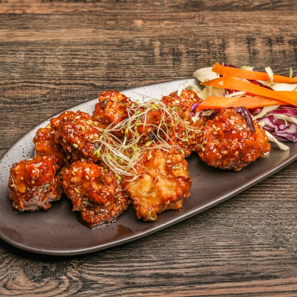 Mumbai Maskaa's Indian-style chicken wings, glazed with sauce and sesame seeds, served with fresh sprouts and slaw.