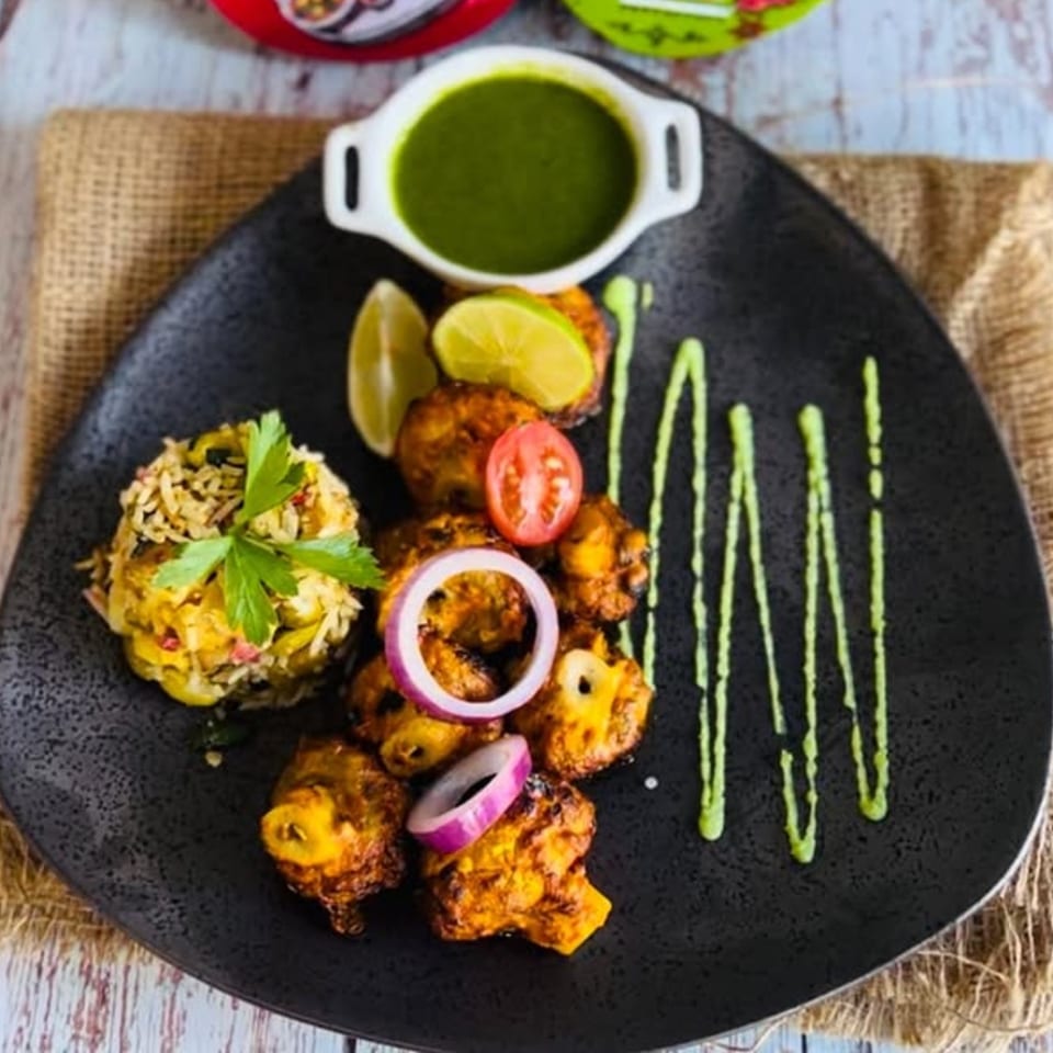 Indian chicken tikka with rice, lime, onion, tomato, and green chutney on a black plate.