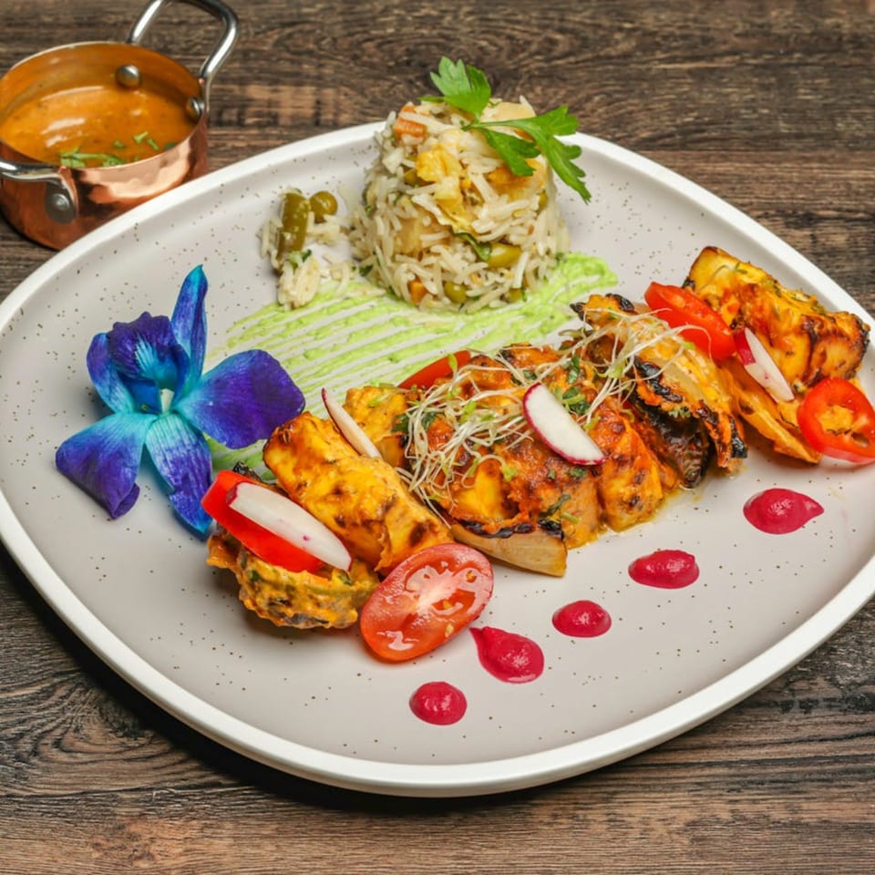 Indian paneer tikka with rice, green sauce, and a blue orchid on a white plate.